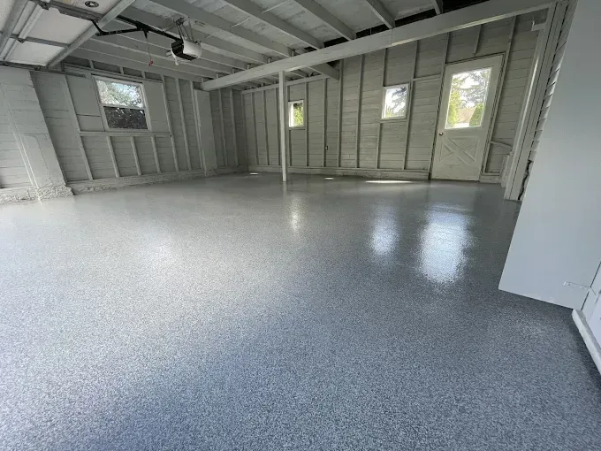 Empty garage with a light grey flake floor and windows along the wall